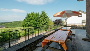 Eine Terrasse mit Picknicktischen und einem Sonnenschirm, mit Blick auf ein bewaldetes Gebiet.