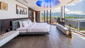 A modern bedroom with a large bed, a cityscape painting, a ceiling with a starry sky design, and a view of a lake and mountains. - Cami Riverside Resort Đà Nẵng (Da Nang)