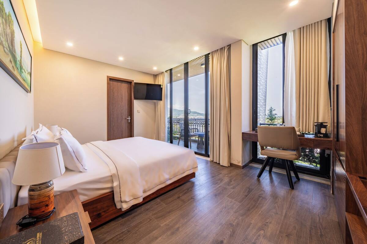 A hotel room with a bed, a desk, a chair, a TV, and a large window with curtains.