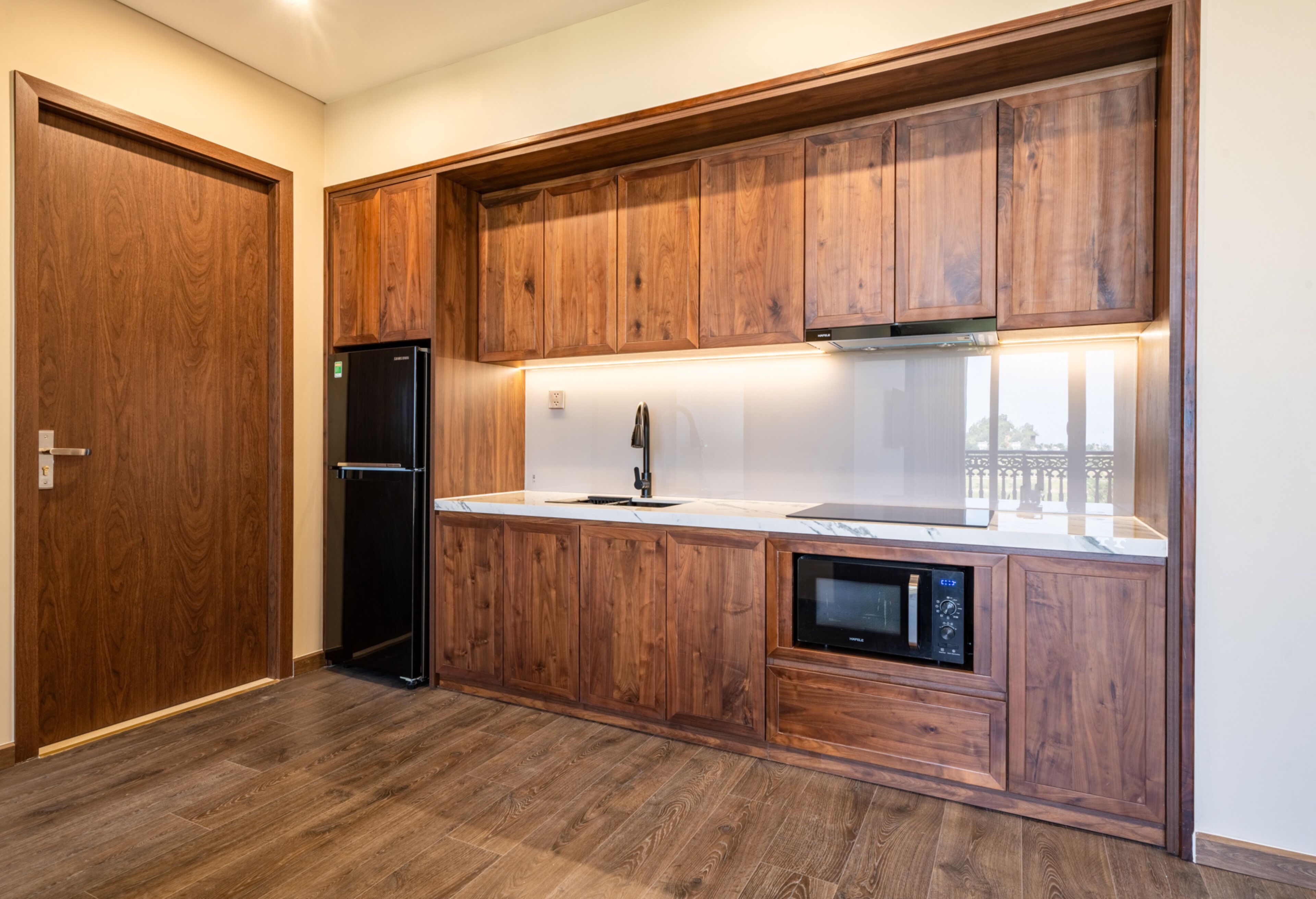 A modern kitchen with wooden cabinetry, a built-in microwave, and a stainless steel refrigerator.