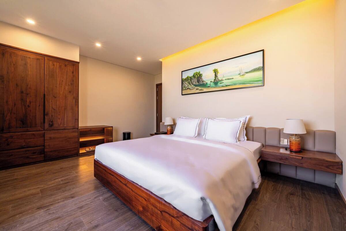 A bedroom with a large bed, wooden wardrobe, and a painting of a beach scene.