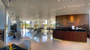 A modern hotel reception area with a wooden reception desk, a reception sign, and a view of the outdoor seating area. - Cami Riverside Resort Đà N ẵng (Da Nang)