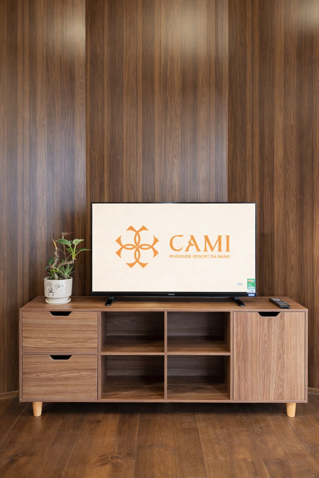 A wooden TV stand with a flat-screen TV displaying the logo "CAMI Riverside Resort Da Nang".
