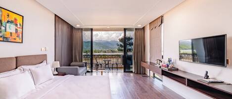 A modern hotel room with a large bed, a TV, a balcony with a view of mountains, and a dining area.