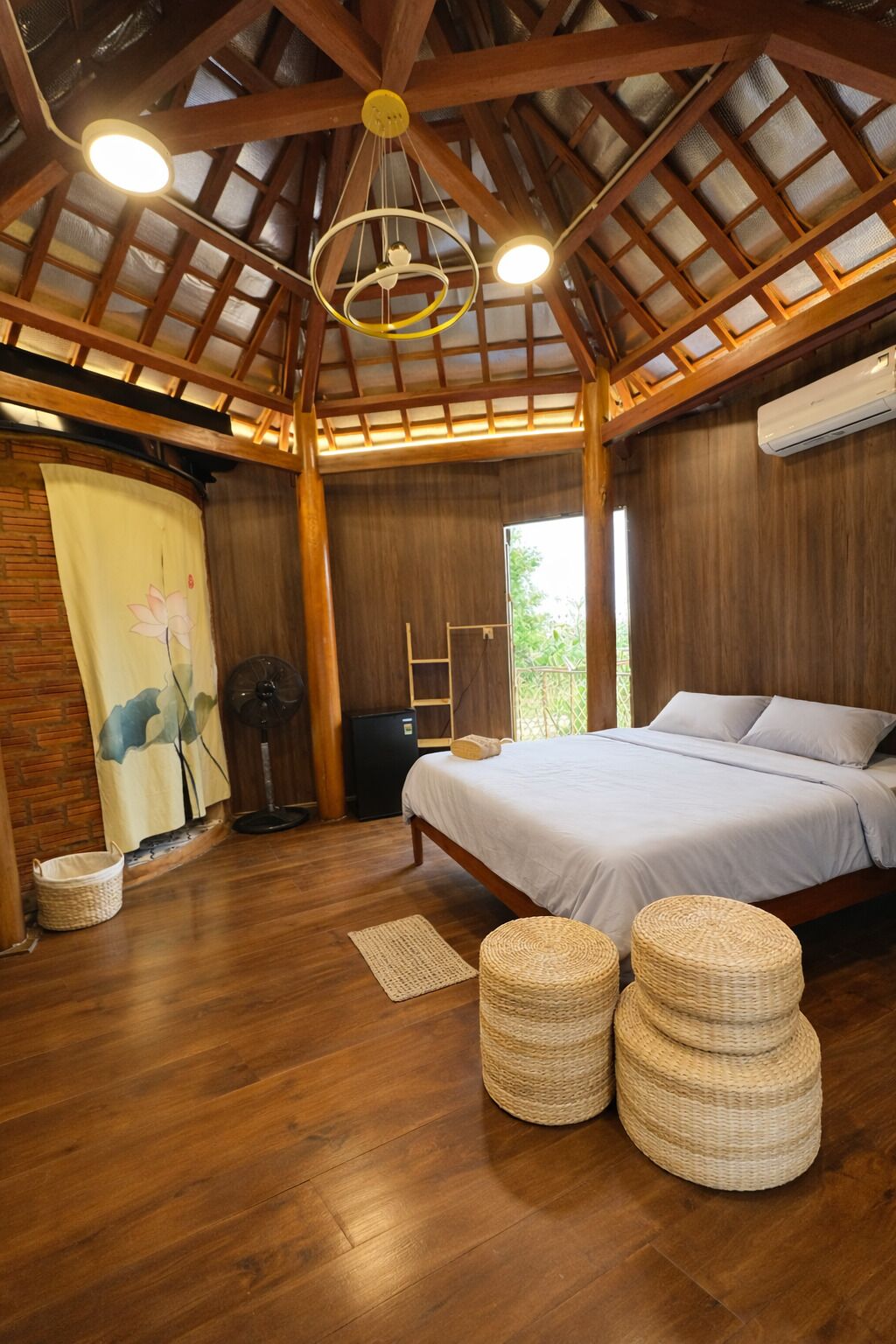 Un dormitorio con techo de madera, una cama, un ventilador, una mesita pequeña y una ventana.