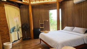 Un dormitorio con techo de madera, una cama, un ventilador, una mesita pequeña y una ventana.