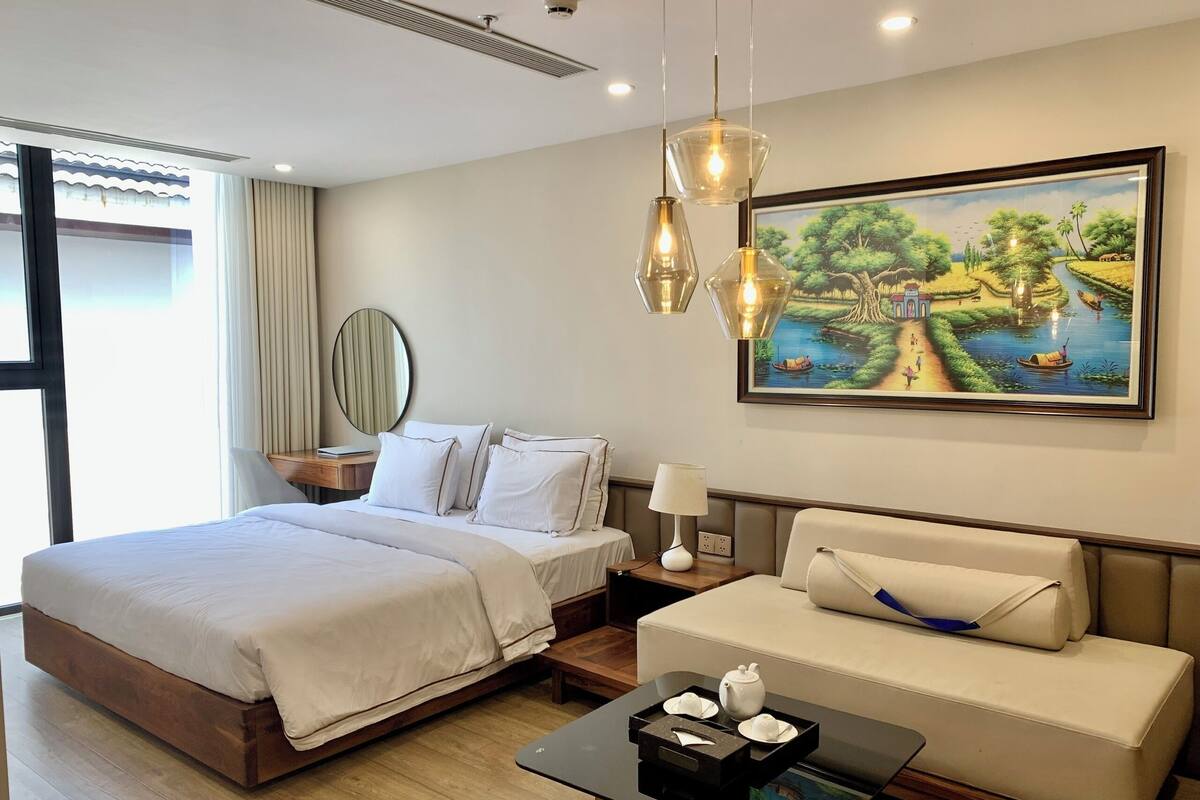 A hotel room with a bed, a sofa, a painting, and a coffee table.