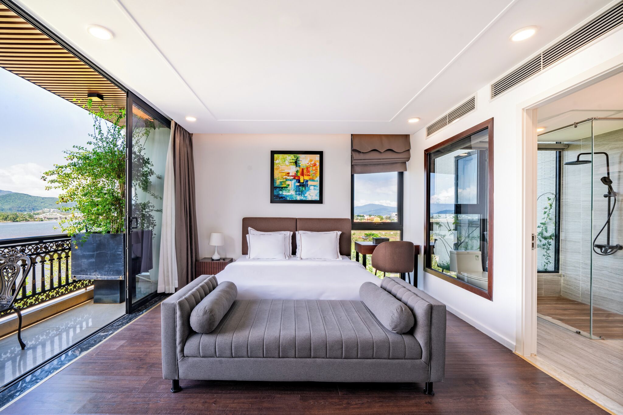 Una habitación de hotel moderna con una cama grande, un sofá, ducha de vidrio y un balcón con vistas a las montañas.