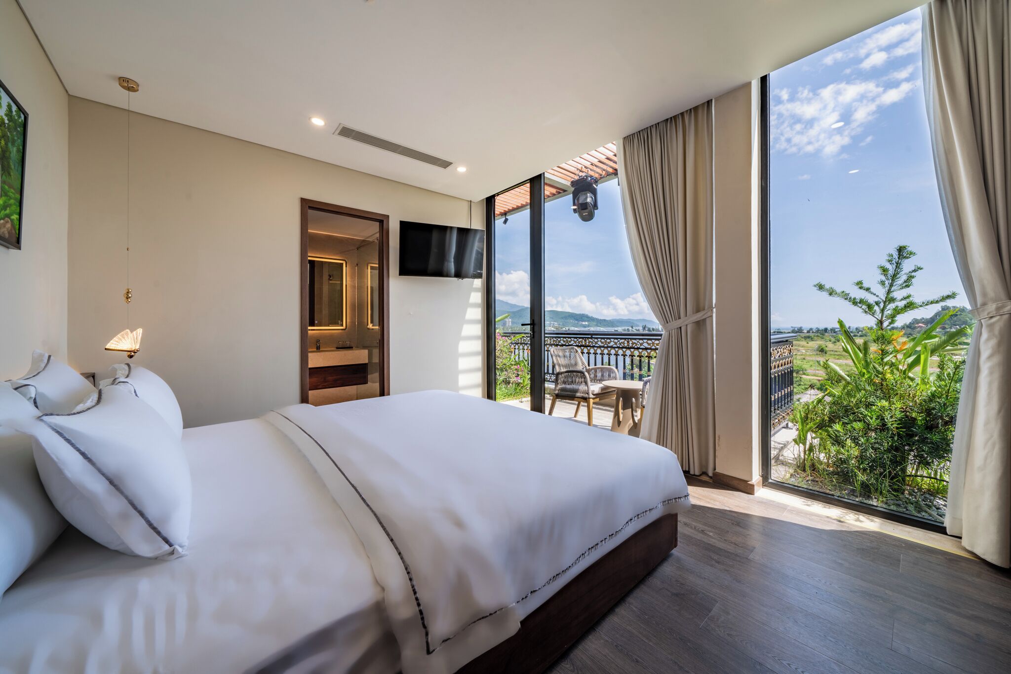 A modern hotel room with a large bed, a TV mounted on the wall, and a balcony with a view of the city.