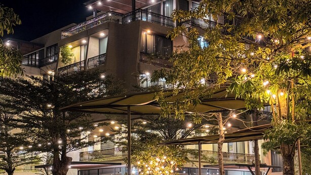 A multi-story building with balconies, a covered outdoor area with string lights, and a well-maintained garden. - Cami Riverside Resort Đà Nẵng (Da Nang)