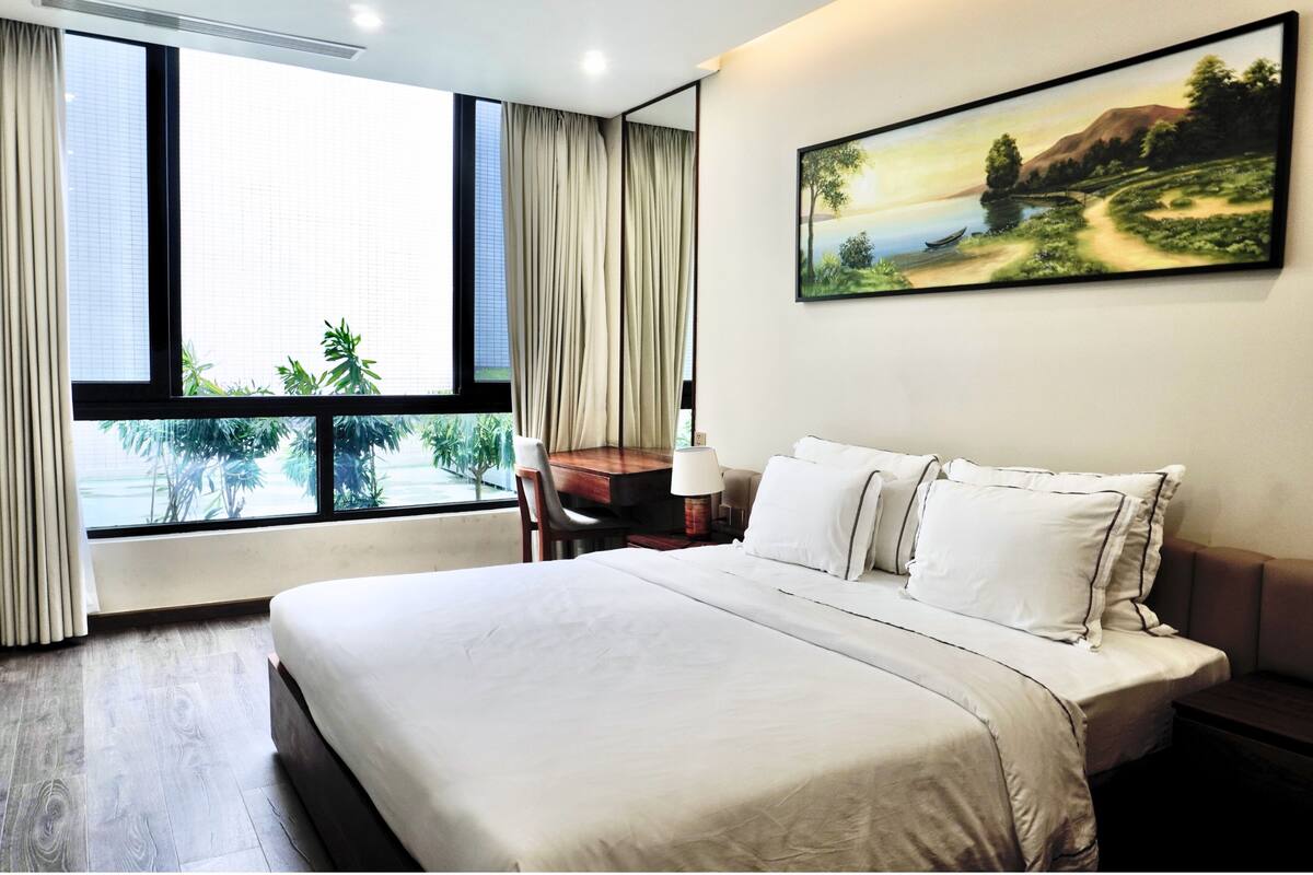 A hotel room with a large bed, a desk, a chair, and a window with curtains.