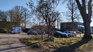 A parking lot with several cars and a white van. There are trees and buildings in the background. - Large loft apartment, private entrance, e-charging station and free parking space (Schwerin)