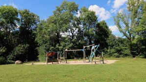 A playground with swings, slides, and climbing structures in a grassy park area with trees in the background. - Large loft apartment, private entrance, e-charging station and free parking space (Schwerin)