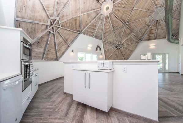 Une cuisine spacieuse avec un haut plafond en bois, un îlot central doté de placards et un four encastré.
