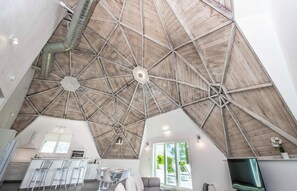 A spacious interior with a high, geometric wooden ceiling, a kitchen area, and a seating space with a view.