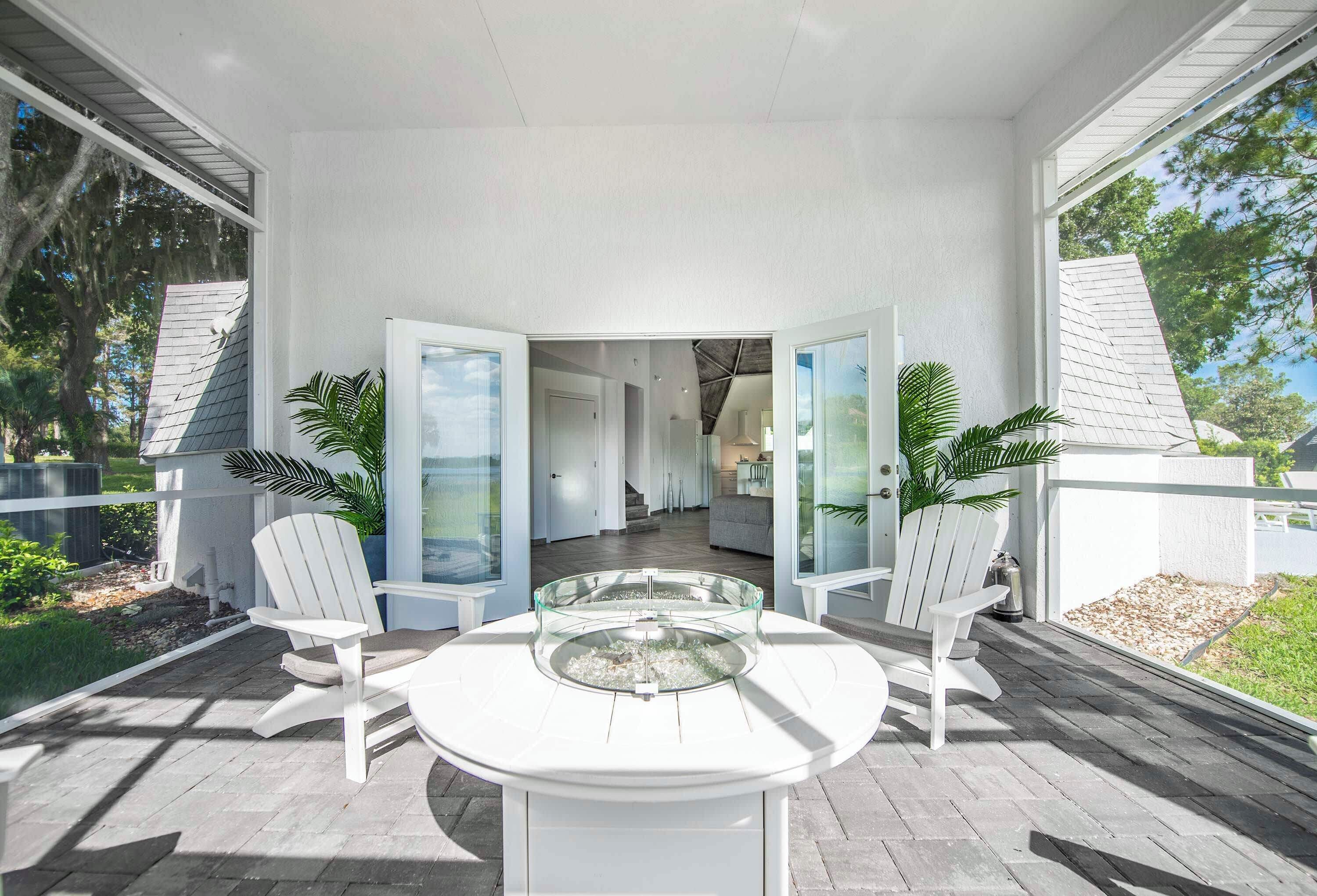 A covered outdoor patio with a glass-top table, white chairs, and a view into the house.