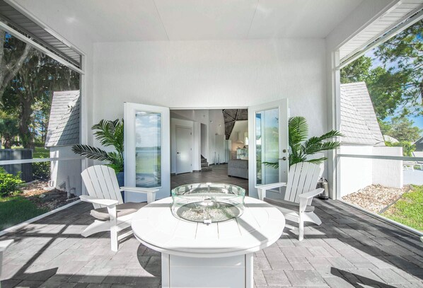 A covered outdoor patio with a glass-top table, white chairs, and a view into the house.