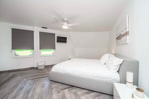 Une chambre moderne avec un lit, un ventilateur de plafond, une fenêtre donnant sur un beau paysage et un téléviseur fixé au mur.