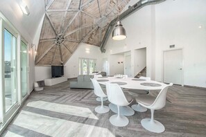 A spacious interior with a high ceiling, a dining area with white chairs and a round table, and a large window providing natural light. - Sumner Lake House 2 Bedrooms (Clermont)