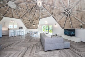 A spacious loft with a high ceiling, a kitchen area, a dining space, and a living room with a large grey sofa. - Sumner Lake House 2 Bedrooms (Clermont)