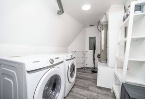 Une buanderie équipée de deux machines à laver Samsung blanches, d’un étendoir et d’un aspirateur.