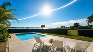 A swimming pool with a view of the ocean, surrounded by palm trees and a well-maintained lawn.