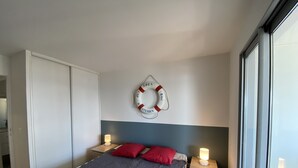 Une chambre à coucher avec un lit, deux tables de chevet avec des lampes, un élément décoratif représentant un dispositif de sauvetage fixé au mur, et une grande fenêtre.
