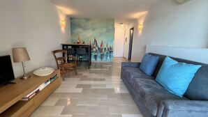 Un salon moderne avec un canapé, un téléviseur, un coin repas avec des chaises et un tableau accroché au mur.
