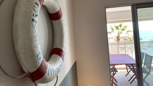 Une bouée de sauvetage accrochée à un mur, un balcon avec une table et des chaises, et une vue sur l’océan.