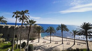 Une promenade en bord de mer, bordée de palmiers, de bancs et d’un mur de pierre d’où l’on peut admirer la mer.