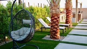 A hanging chair, a bench, and two palm trees in a garden area. - A modern vacation home in Desert Hot Springs, built in 2020 with 4 bd, 3 baths (Desert Hot Springs)