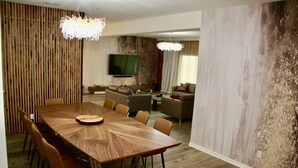 A modern dining area with a long wooden table, multiple chairs, and a television in the background. - A modern vacation home in Desert Hot Springs, built in 2020 with 4 bd, 3 baths (Desert Hot Springs)