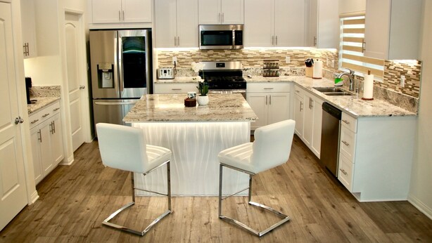 A modern kitchen with white cabinetry, a central island with bar stools, stainless steel appliances, and a tiled backsplash. - A modern vacation home in Desert Hot Springs, built in 2020 with 4 bd, 3 baths (Desert Hot Springs)