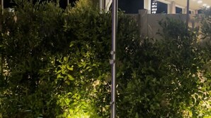 A modern outdoor shower with a metal frame, surrounded by a square gravel area and lush green bushes. - A modern vacation home in Desert Hot Springs, built in 2020 with 4 bd, 3 baths (Desert Hot Springs)