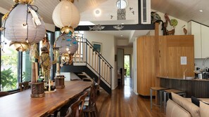A spacious kitchen with wooden cabinets, a dining area with a long wooden table, and a staircase leading to an upper level. - Byron Bay Accom - South Beach House 8 South Beach Lane - Pet Friendly (Byron Shire)