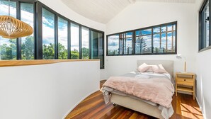 Une chambre avec une grande fenêtre, un lit, une table de chevet et un luminaire suspendu.