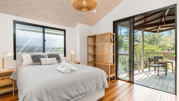 Une chambre dotée d’un grand lit, d’une bibliothèque en bois et d’une porte-fenêtre coulissante donnant sur un espace extérieur avec une table et des chaises.