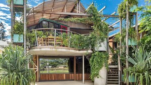 Une maison moderne dotée d’une architecture originale, avec un toit incurvé, une terrasse en bois et une végétation luxuriante.