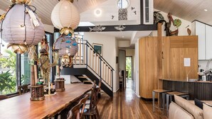 Un grand espace à manger avec une longue table et des chaises en bois, un escalier avec une rampe et une cuisine équipée d’armoires en bois et d’un évier.