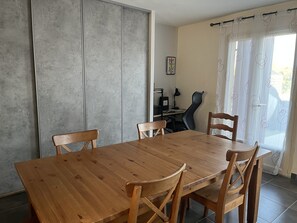 A dining area with a wooden table and chairs, a sliding door, a desk with a chair, and a window with curtains.