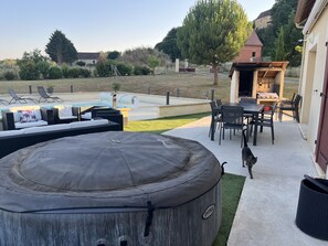 A backyard with a hot tub, outdoor seating, a barbecue area, and a pool.