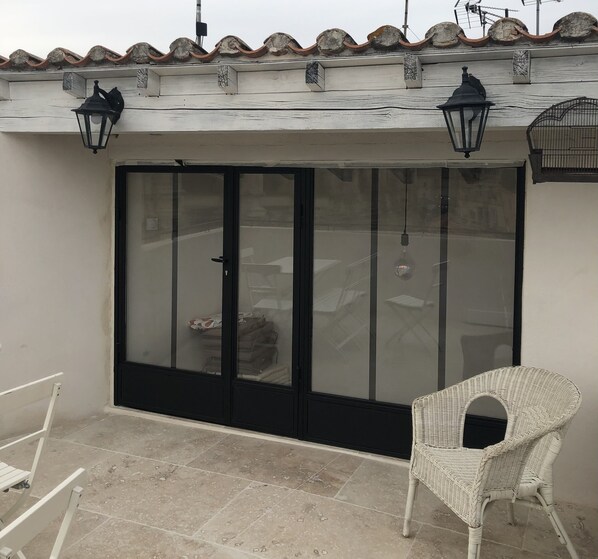 A room with a sliding glass door, a white wicker chair, and two black wall-mounted lamps. - Across from Les Arenes and La Major (Arles)