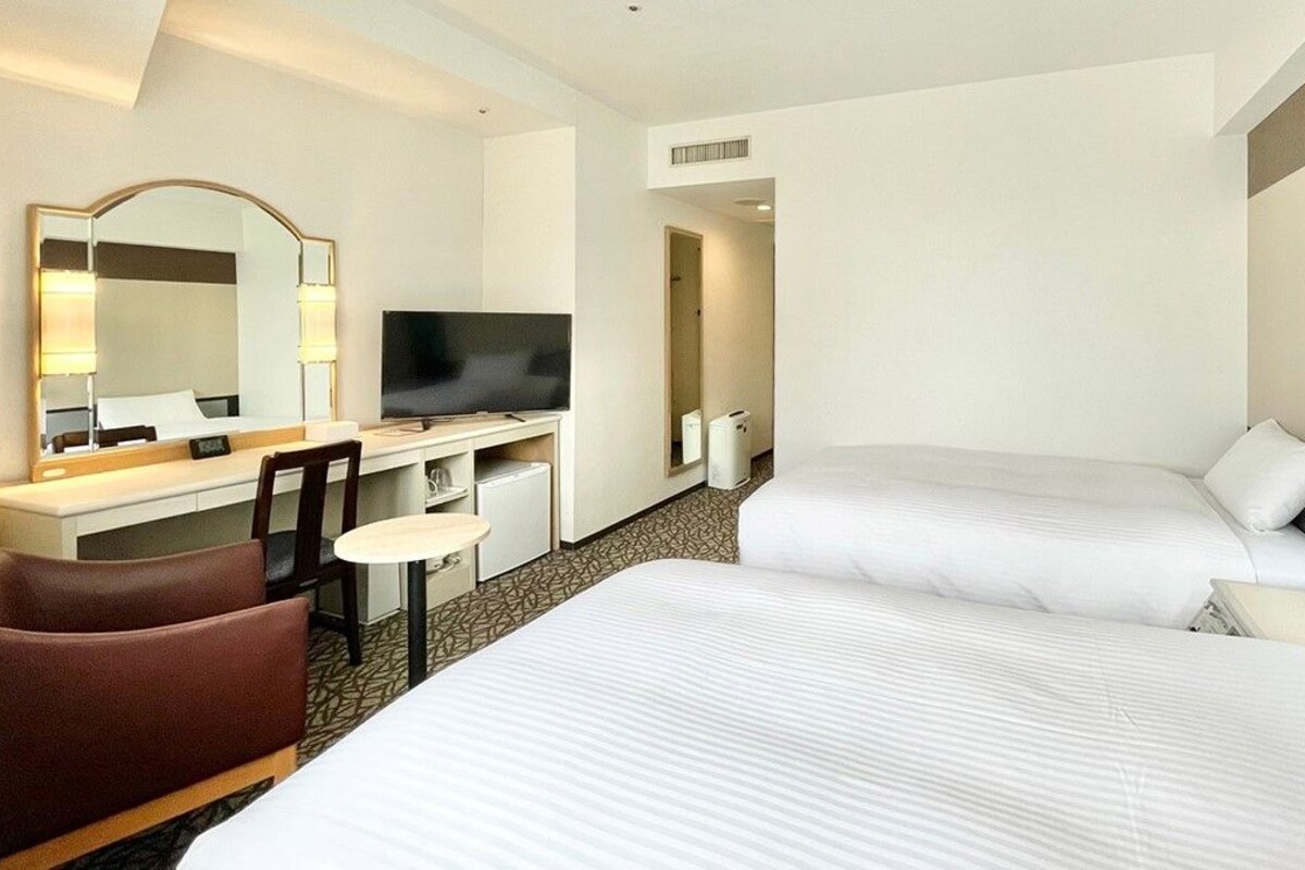 Habitación de hotel con dos camas, un escritorio con televisor, un espejo y una silla.