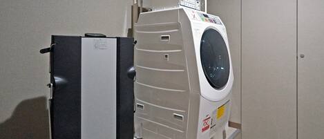 Un lavadero compacto y moderno con lavadora y secadora de carga frontal, un panel de control y un refrigerador pequeño.