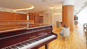 A grand piano in a spacious room with wooden flooring, a high ceiling with recessed lighting, and a large column. - Chisun Hotel Yokohama Isezakicho (Yokohama)