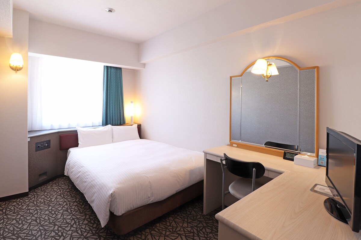 Habitación de hotel con cama, escritorio, silla y un espejo grande.