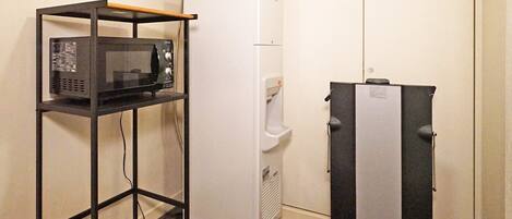 Una kitchenette compacta con un microondas en un estante, un refrigerador y un mini refrigerador.