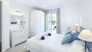 Une chambre avec un grand lit, une commode blanche, un miroir et une vue sur l’extérieur.