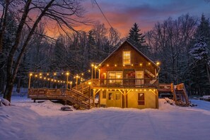 Una cabaña de madera con balcón, rodeada de árboles cubiertos de nieve.