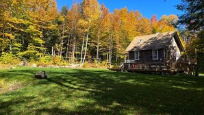A cabin with a deck, surrounded by a forest with autumn foliage. - Dream Stratton Forest Cabin w/Hot Tub & Fast WiFi (Stratton)